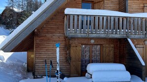 A wooden cabin with a balcony, a ski lift, and a bed covered in snow.
