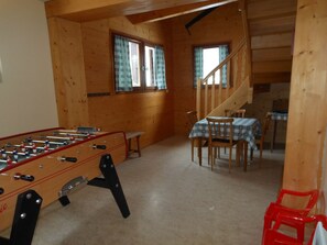 Un interior de madera con una mesa de fútbol, una mesa de comedor con sillas y una escalera.
