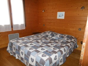 Una cama individual con colcha estampada en una habitación de madera con ventana y un cuadro pequeño en la pared.