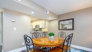 A dining area with a round wooden table, black metal chairs, a small potted plant, and a blue patterned rug.