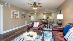 A living room with a brown leather sofa, a glass coffee table, and a ceiling fan.