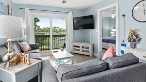 Un salon moderne avec un canapé, une table basse et un téléviseur. Il y a un balcon avec vue sur l’extérieur.