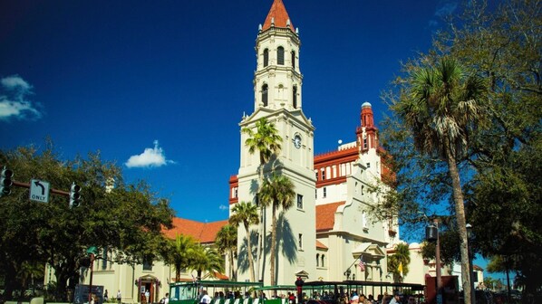 A historic building with a clock tower, palm trees, and a clear blue sky.