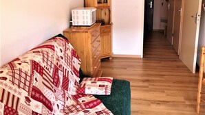 A cozy room with a wooden dresser, a bed with a patterned blanket, and a hallway leading to a door. - Cozy studio 4 pers, piste view, La Joue du Loup (La Joue du Loup)