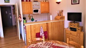 A kitchen with wooden cabinets, a microwave, a sink, and a dining area with a table and chairs. - Cozy studio 4 pers, piste view, La Joue du Loup (La Joue du Loup)
