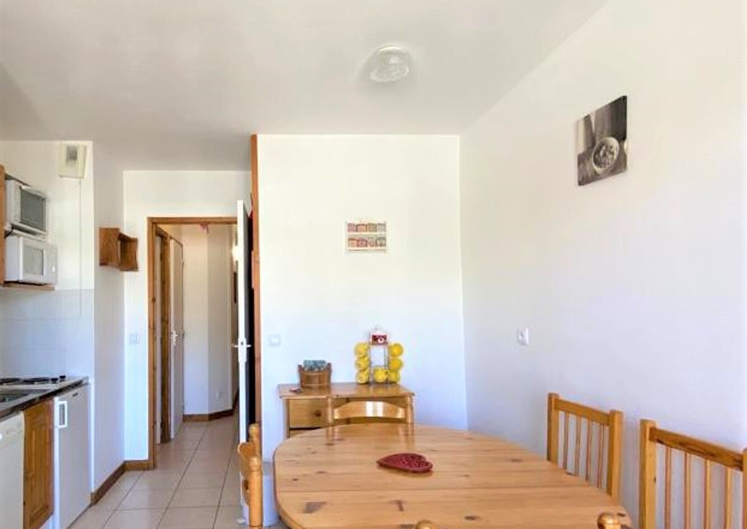 A dining area with a wooden table and chairs, a kitchen with a microwave and cabinets, and a hallway leading to another room.
