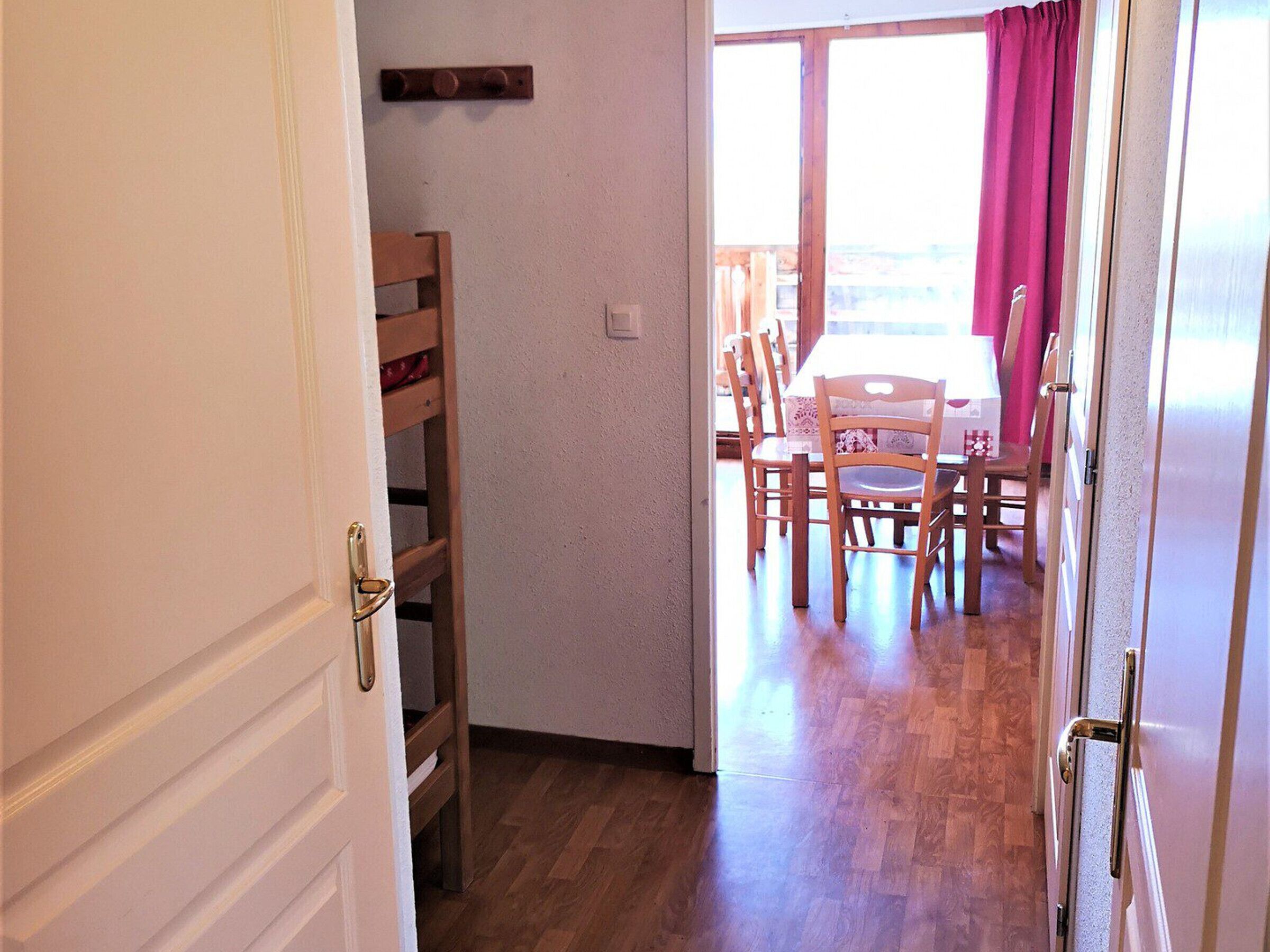 An interior hallway with a wooden chair, a table with a tablecloth, and a view through a window with curtains.