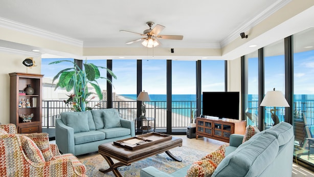 A spacious living room with a large window overlooking the ocean, a ceiling fan, and a television.