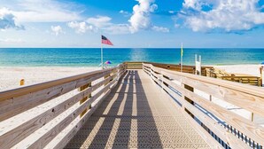 A wooden pier leading to a beach with an American flag.