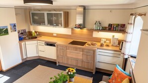 A compact kitchen with a central island, a built-in oven, and a microwave. There is a sink with a faucet, and the kitchen has wooden cabinets.