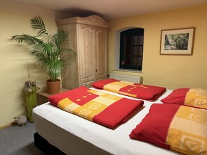 Ein Schlafzimmer mit einem Bett, einem Blumentopf, einem Kleiderschrank, einem Fenster und einem Bild an der Wand.