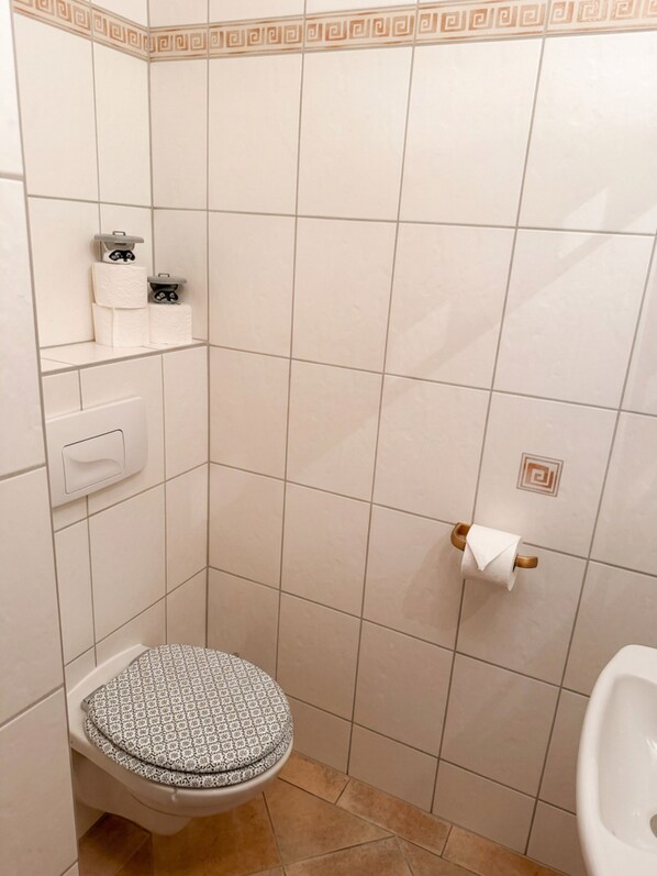 A small bathroom with a toilet, a shelf with toilet paper, and a towel rack.
