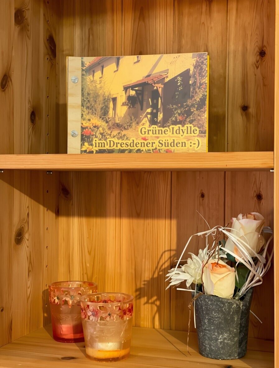 A wooden shelf with a book titled 'Grüne Idylle im Dresdner Süden' and two candle holders with floral designs.