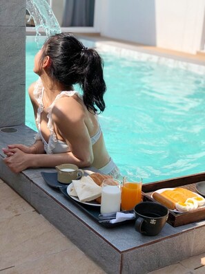 A woman relaxing by a poolside with a tray of breakfast items including toast, eggs, juice, and coffee. - Amadha Pool Villas (Krabi)