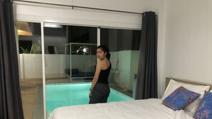 A bedroom with a bed, a nightstand, and a view of a swimming pool through a glass door.