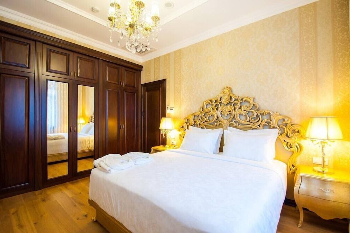 A hotel room with a large bed, wooden wardrobe, chandelier, and two bedside lamps.