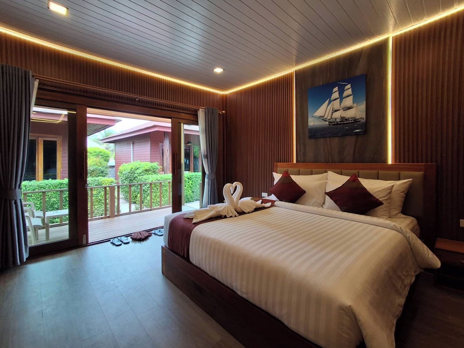 Une chambre d’hôtel avec un grand lit, une vue sur l’extérieur et un tableau représentant un voilier.
