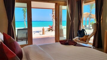 A hotel room with a large bed, a view of the beach, and a chair with a bag.