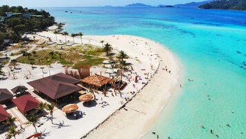 A beach resort with thatched-roof huts, a sandy beach, and clear turquoise waters.