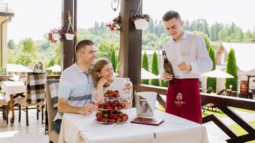 A dining area with a table set for three, a three-tiered strawberry dessert, and a waiter holding a bottle.