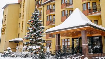 Un hôtel dont l’entrée est recouverte de neige, avec un sapin de Noël et des places assises à l’extérieur.