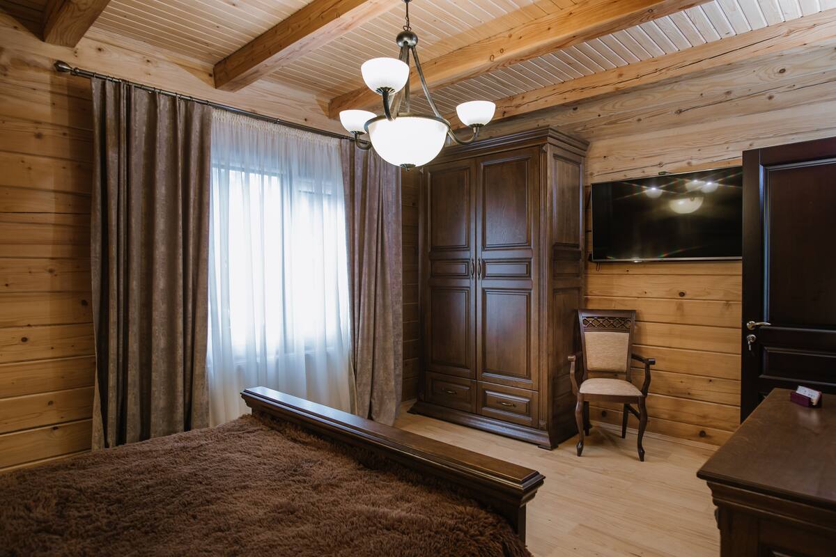 Ein Zimmer mit Holzwänden und -decke, einem großen Bett, einem Kleiderschrank, einem Stuhl und einem an der Wand befestigten Flachbildfernseher.