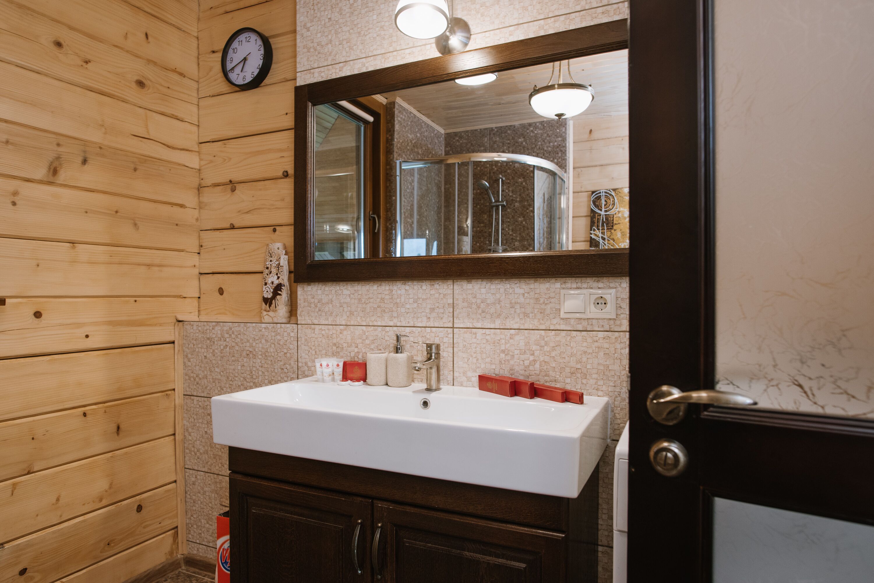 A bathroom with wooden walls, a white sink, a mirror, and a clock.