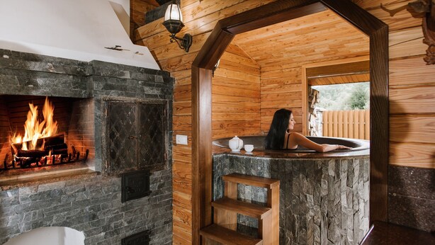 Interior de una cabaña de troncos con chimenea de piedra, un jacuzzi y una escalera de madera.