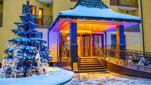 Entrada de un hotel con tejado nevado, un árbol de Navidad y luces festivas.