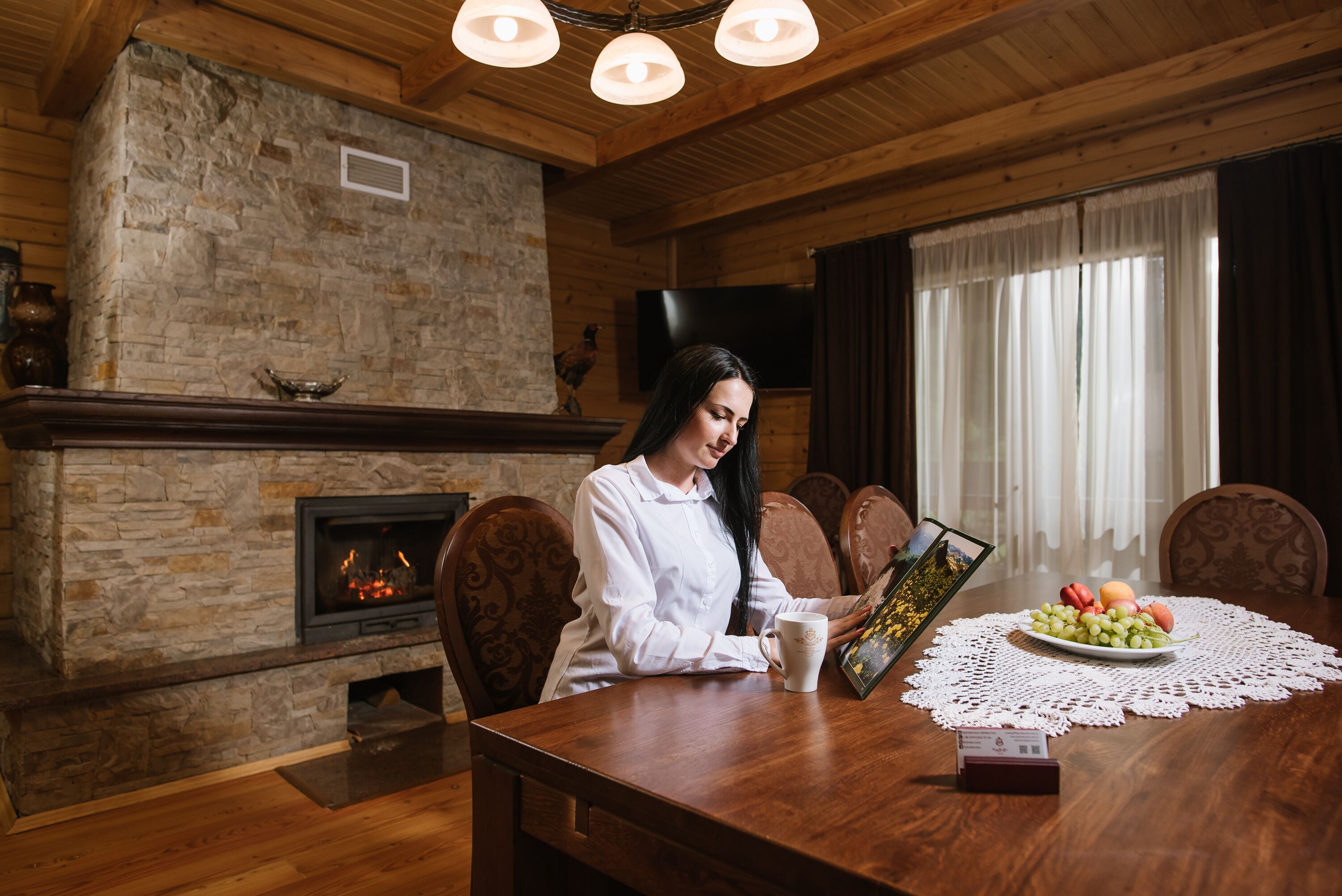 A cozy dining area with a stone fireplace, wooden ceiling, and a television mounted on the wall.