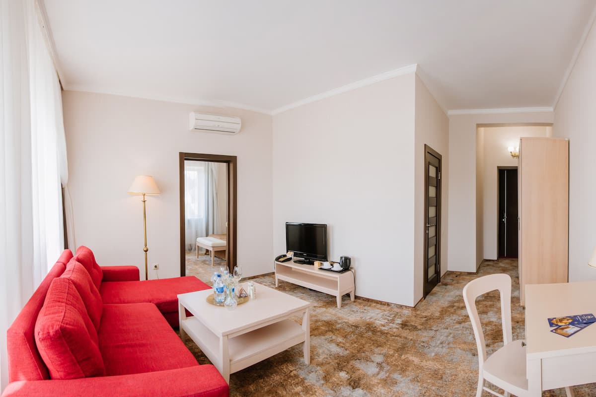 Ein Hotelzimmer mit rotem Sofa, Fernseher, Schreibtisch mit Lampe und Spiegel.