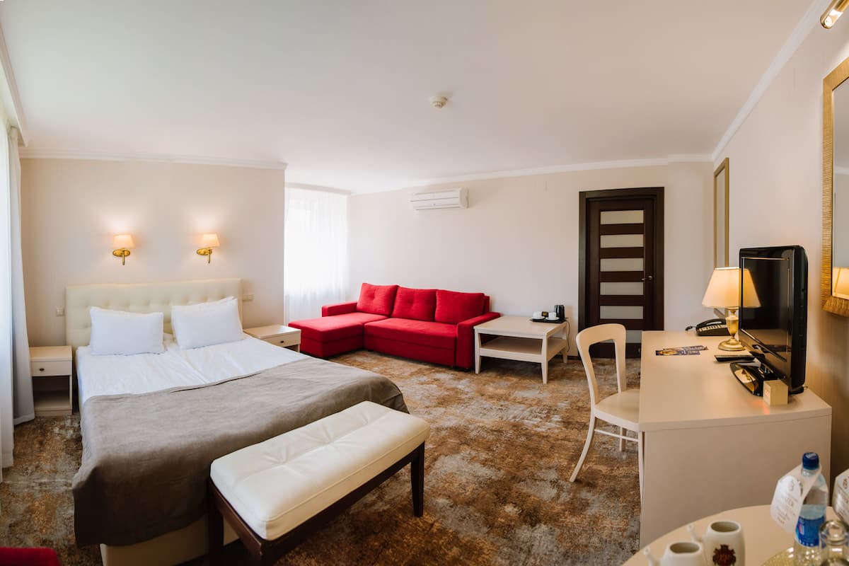 Ein Hotelzimmer mit einem Bett, einem roten Sofa, einem Schreibtisch, einem Sessel und einem Fernseher.