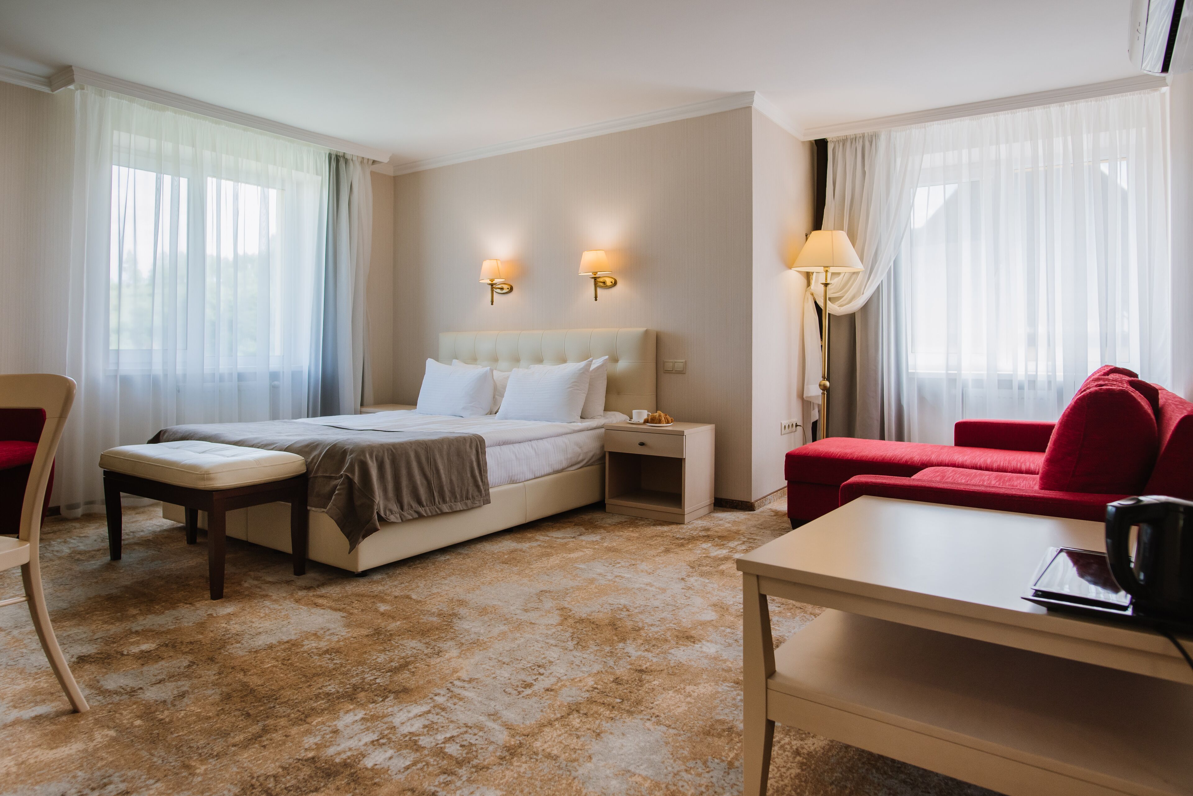 A hotel room with a bed, a red sofa, a small table, and a nightstand.