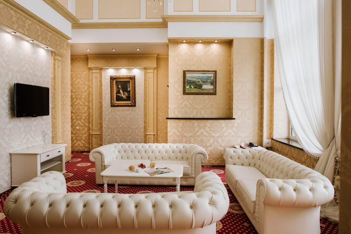 Ein luxuriöses Wohnzimmer mit einem roten Teppich mit Muster, weißen Sofas, einem weißen Couchtisch und einem flachbildfernseher an der Wand.
