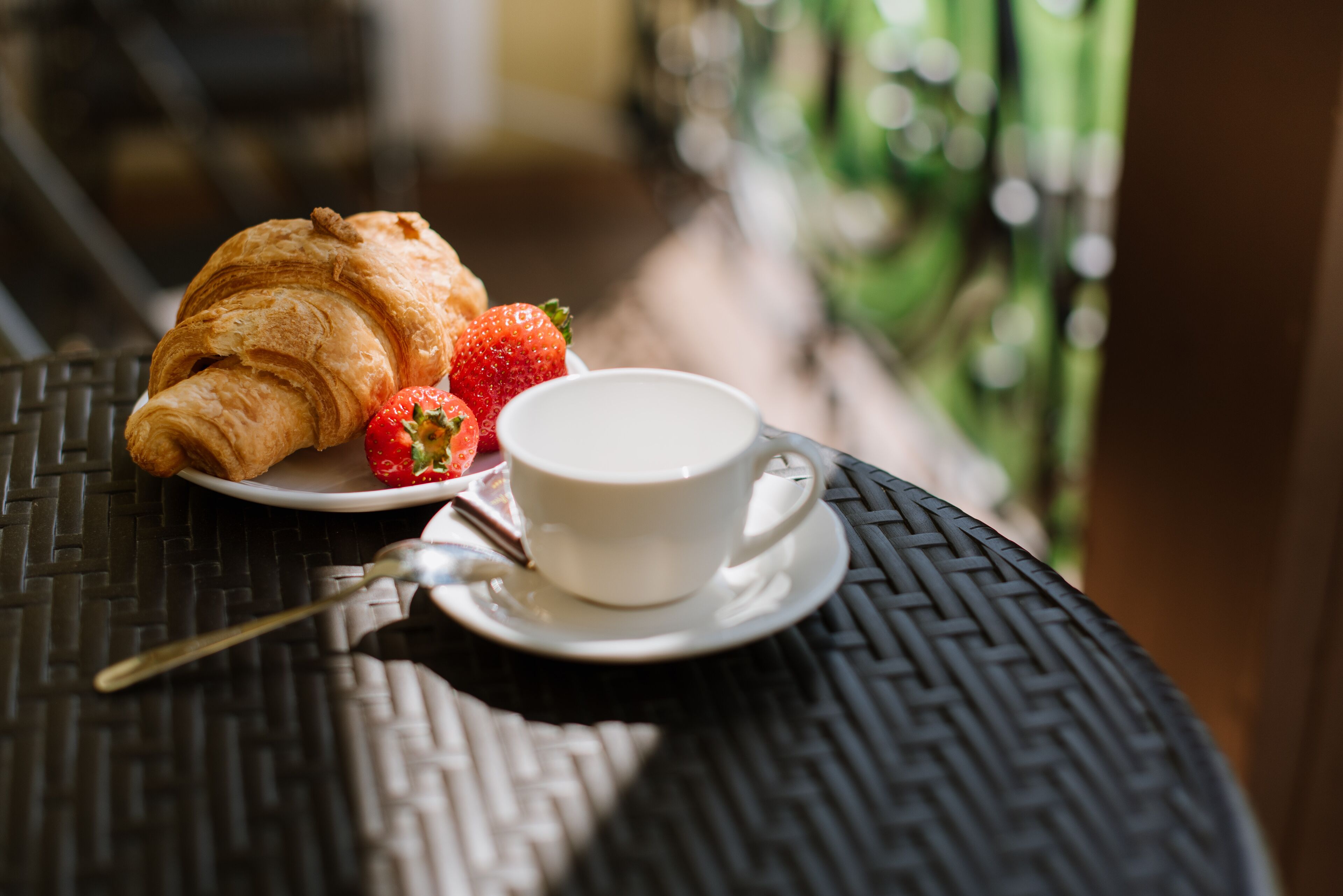 Un croissant, una fresa y una taza de café sobre una mesa.