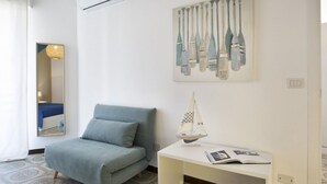 A room with a bed, a desk with a book, a wall-mounted painting, and a mirror.