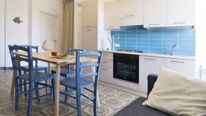 A compact kitchen with blue tiles, a dining area with blue chairs, and a patterned rug.