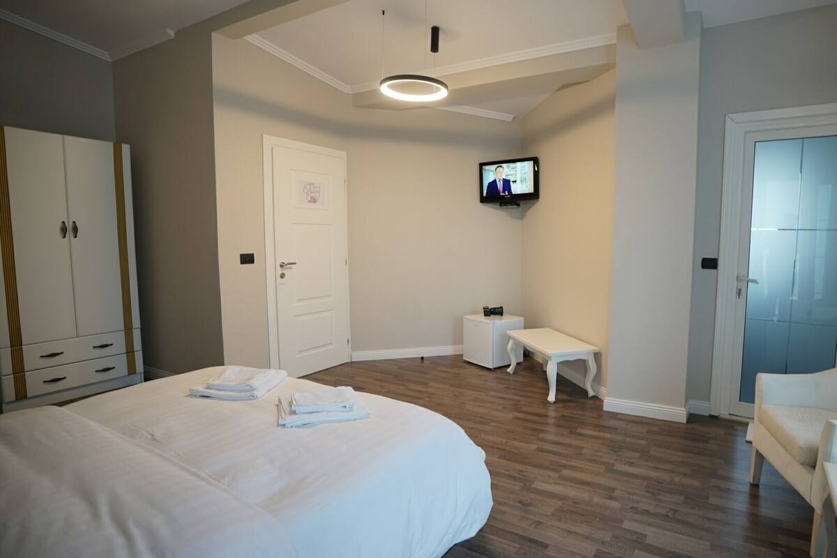 A hotel room with a bed, a chair, a small table, a television, and a wardrobe.