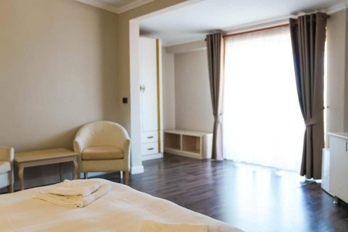 A hotel room with a bed, two chairs, a small table, a wardrobe, and a window with curtains.