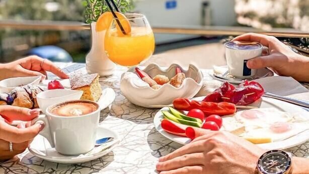 A table set with breakfast items, including pastries, a glass of orange juice, and a cup of coffee, overlooking a beach. - Hotel Majestic (Durrës)