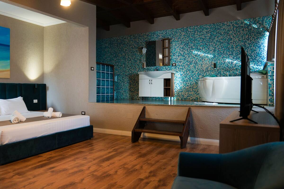 A hotel room with a bed, a desk, a chair, a bathroom with a tiled backsplash, and a painting on the wall.