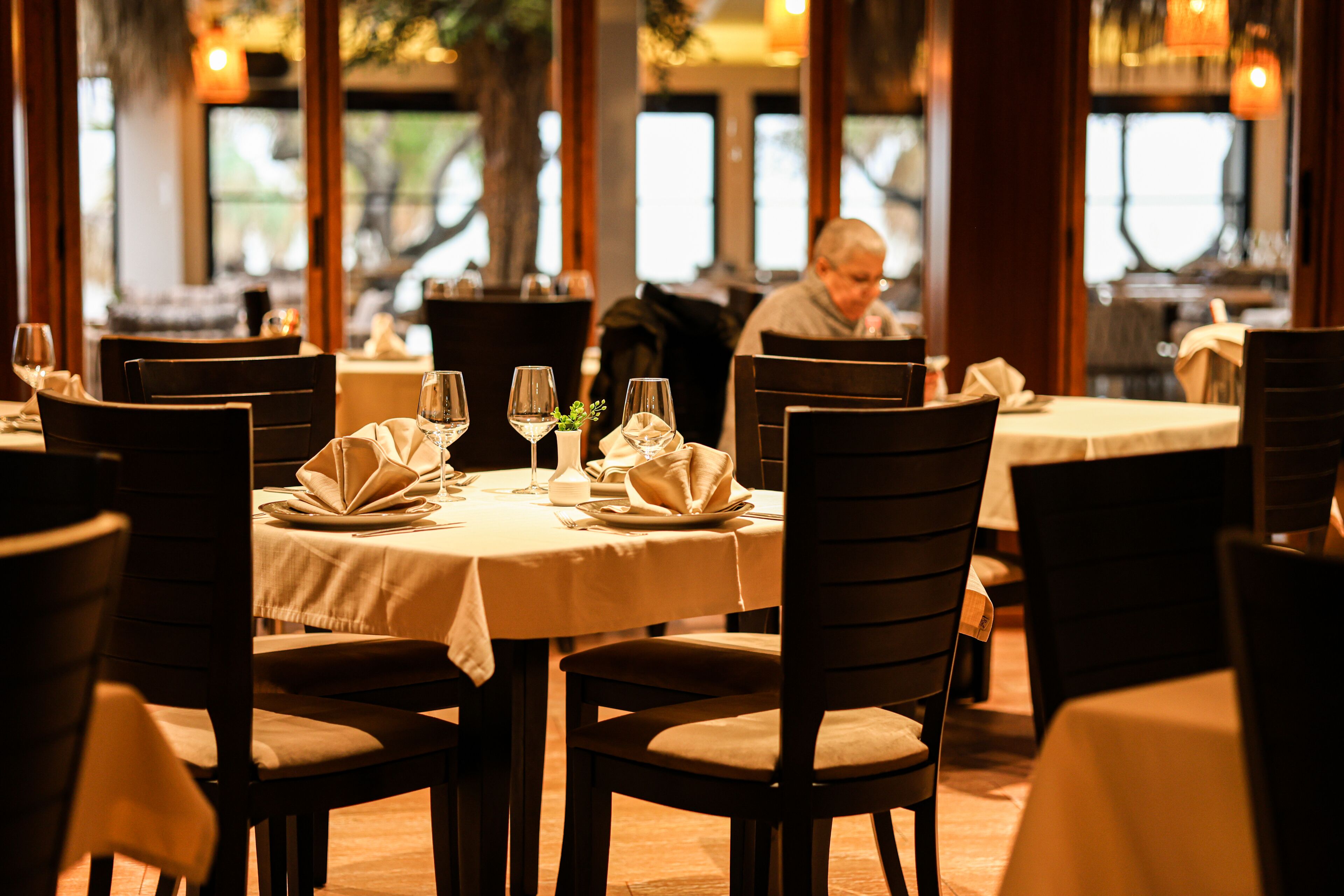 A restaurant with round tables, dark chairs, and neatly set dining tables with wine glasses and folded napkins.