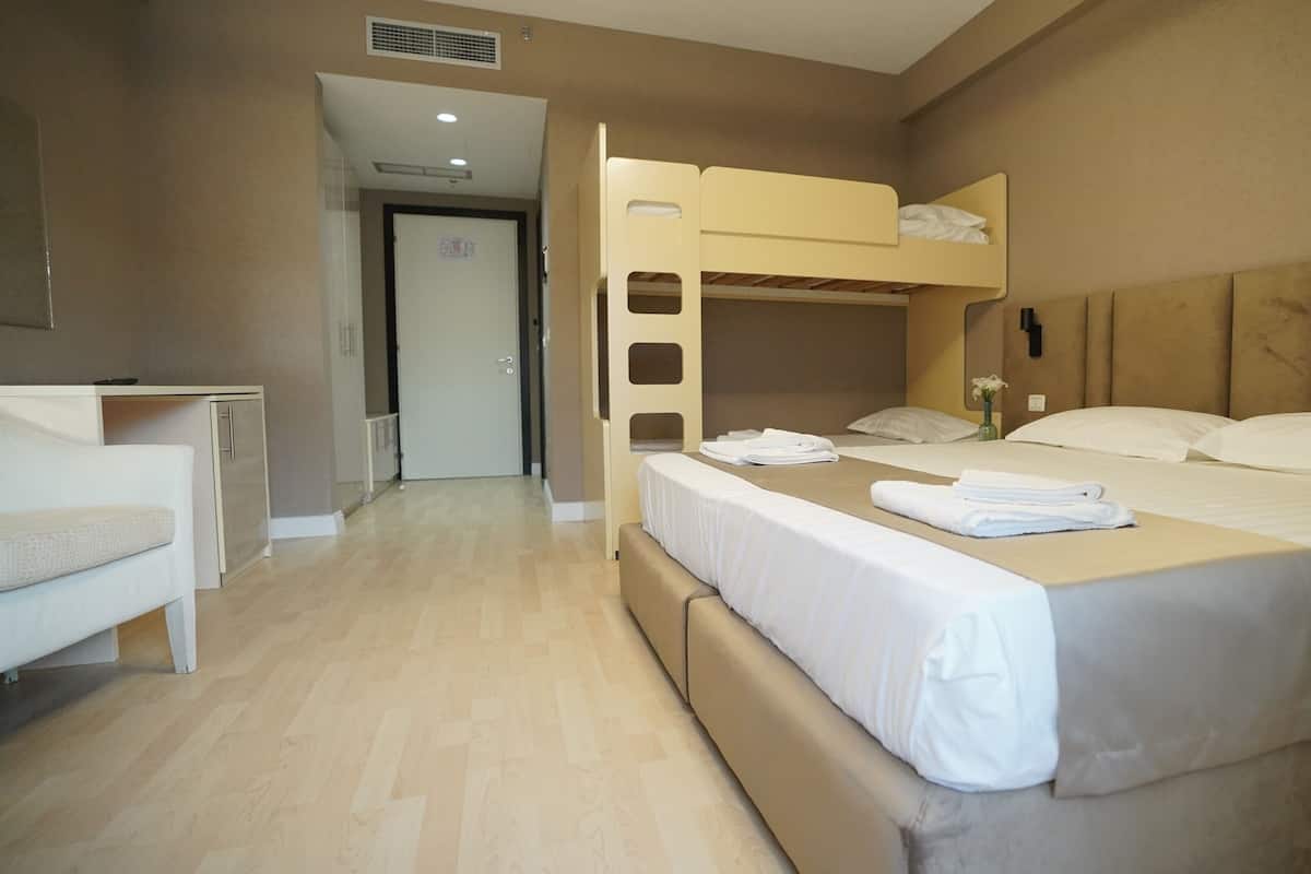 A hotel room with a bunk bed, a single bed, a desk, and a chair.