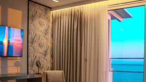 A modern hotel room with a large bed, a chair, a TV, and a balcony with a view of the sea. - Hotel Majestic (Durrës)
