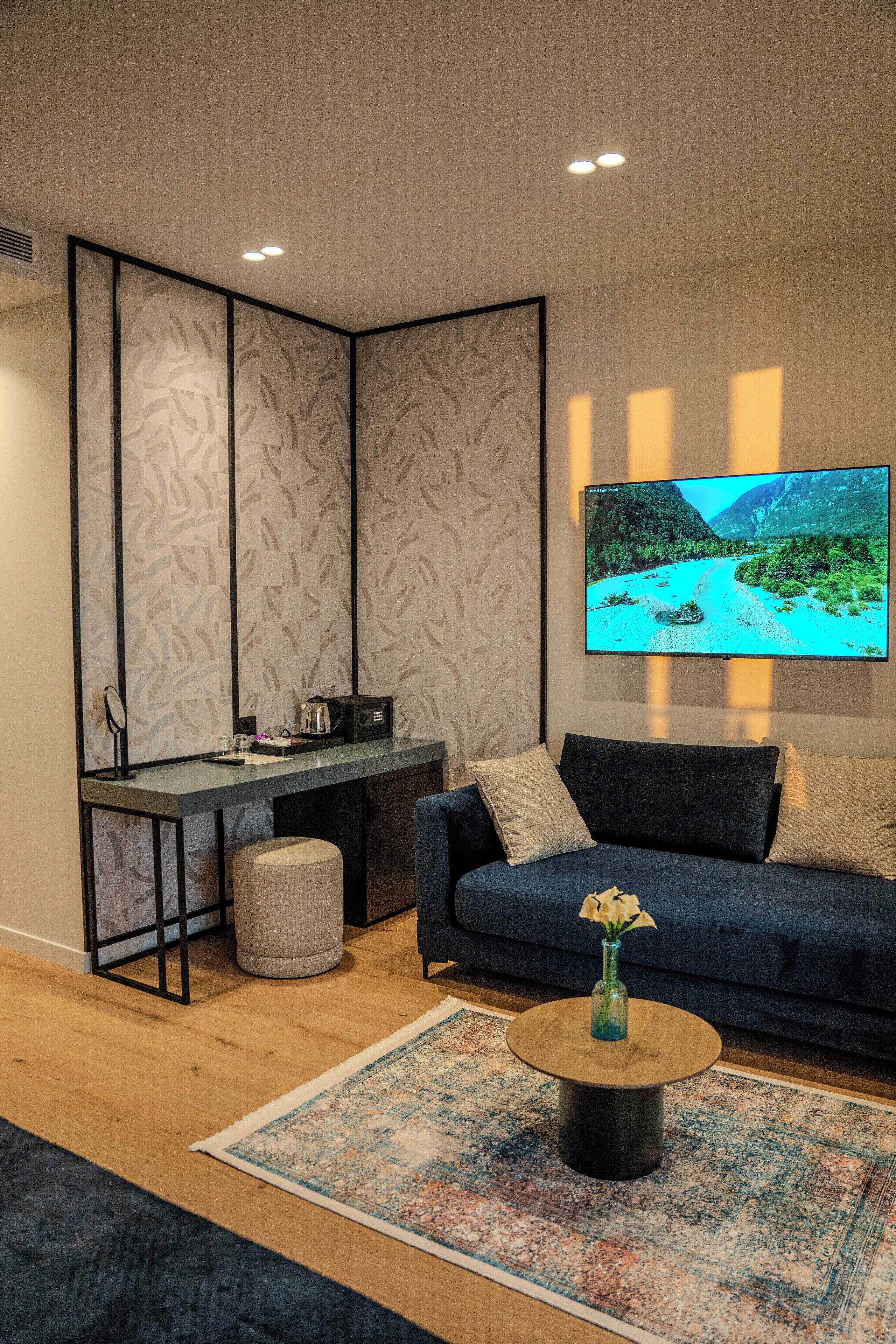 Una sala moderna con un sofá azul oscuro, una mesa de centro con un florero, un televisor de pantalla plana en la pared y un escritorio con una silla.
