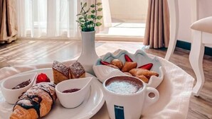 A breakfast tray with pastries, a cup of coffee, and a small plant on a table by a window with curtains. - Hotel Majestic (Durrës)