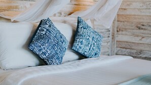 Una cama con ropa blanca y almohadas de estampado azul, un dosel y una pared con una obra de arte floral.