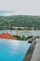 Uma piscina com um deck de madeira, uma ponte e um morro coberto de vegetação ao fundo.