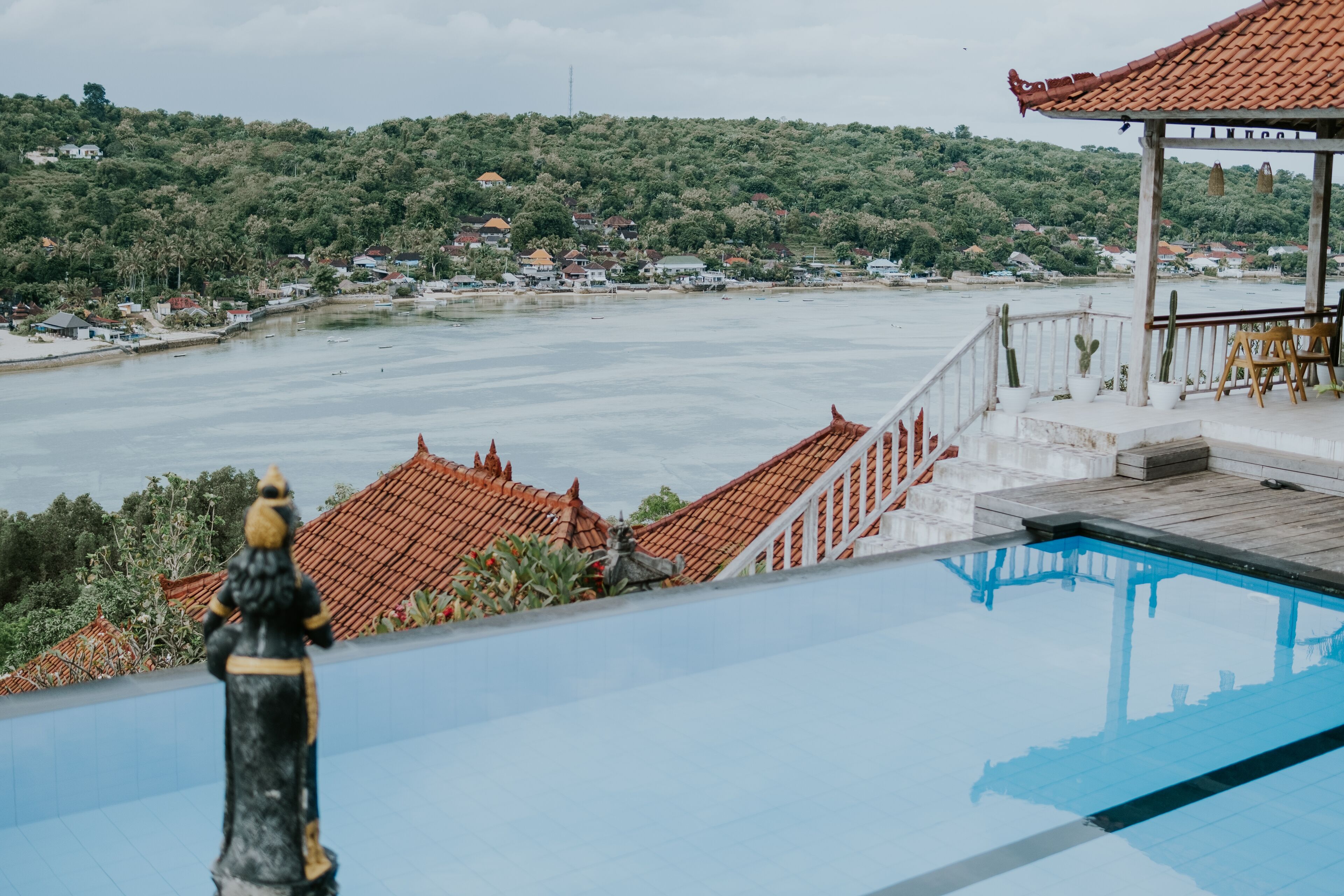 Un espace piscine offrant une vue sur une ville côtière, un belvédère et une statue.