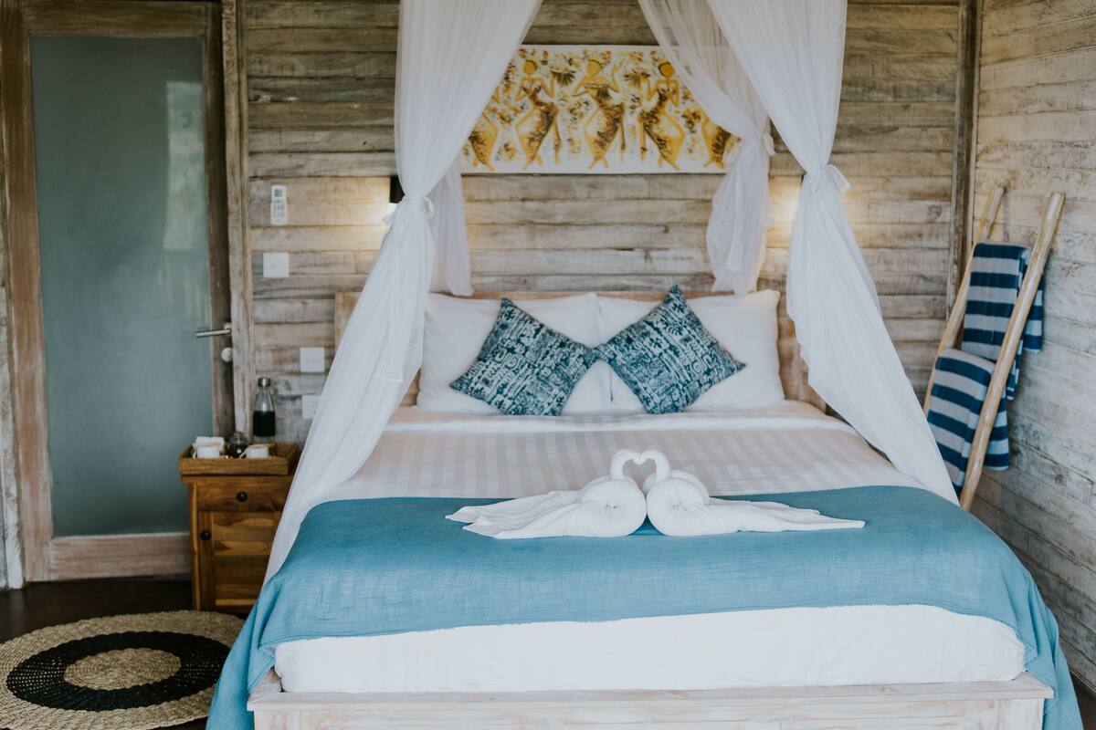 Een bed met hemelbed, gestreepte kussens en een blauwe sprei.